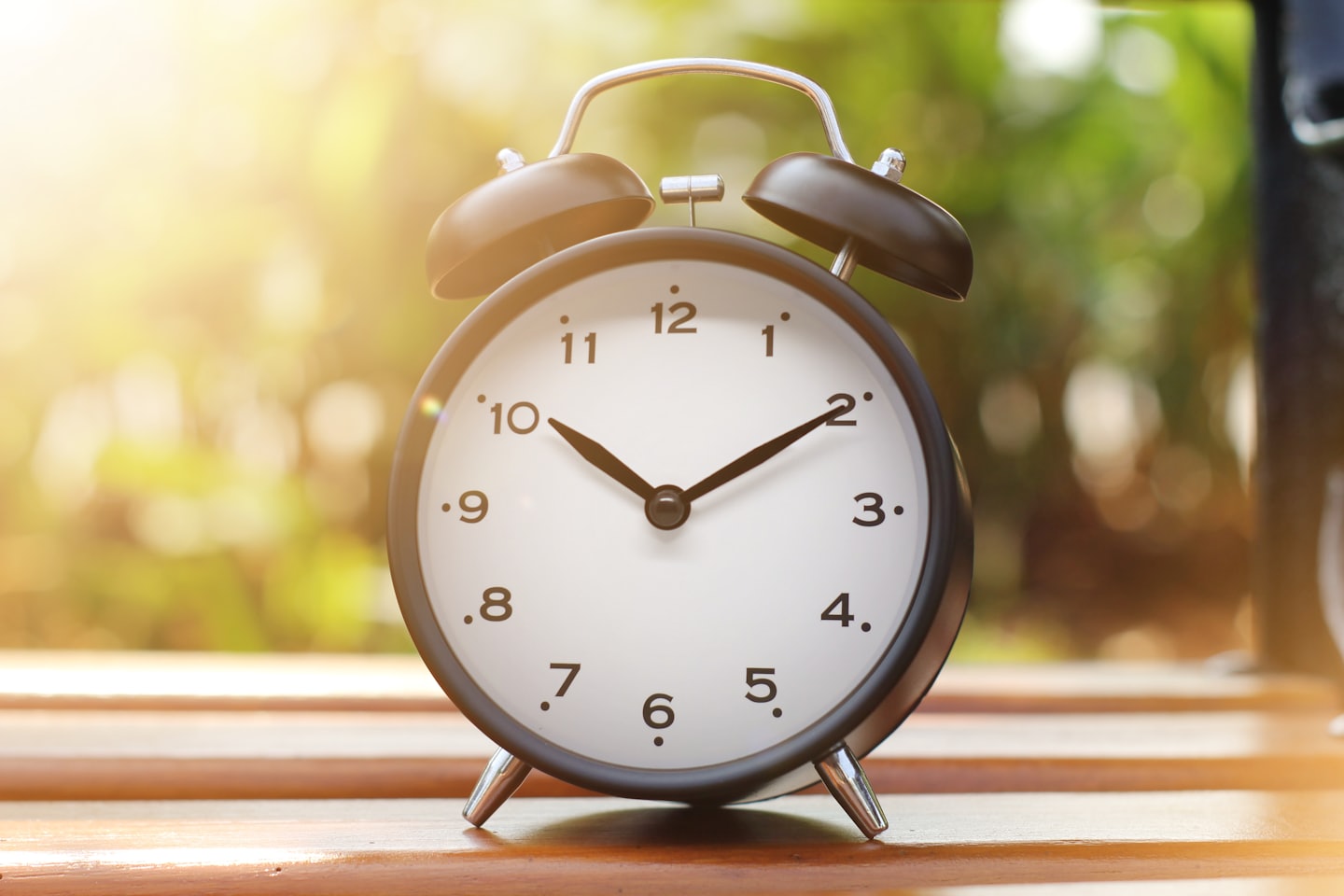 AGWAT black alarm clock on a wooden bench in morning sunlight, symbolizing time awareness and taking action today.